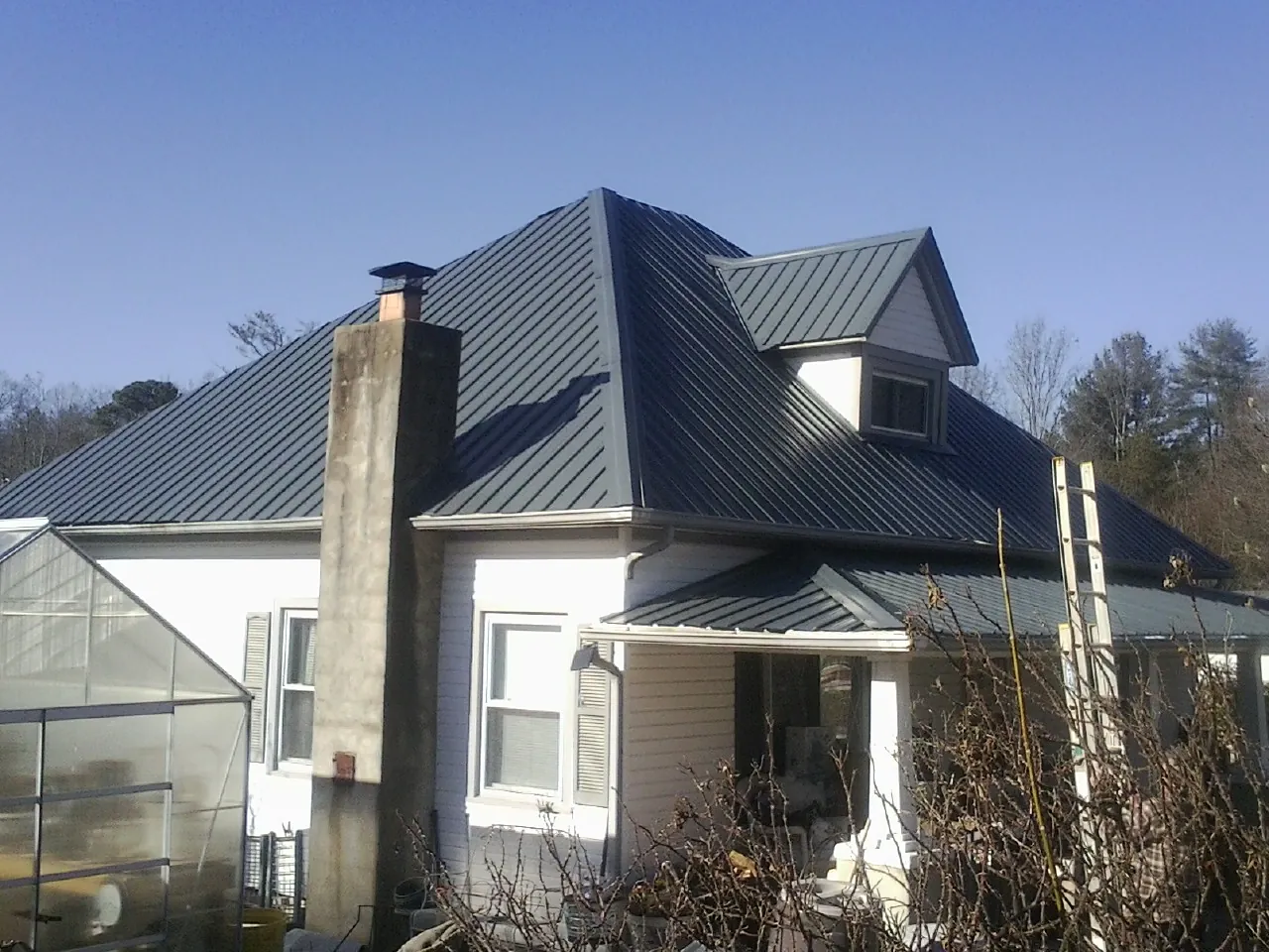 Dark blue standing seam metal roof on a white farmhouse with dormer — Slate & Tile Roof Repair by Roofing Brothers in Newton