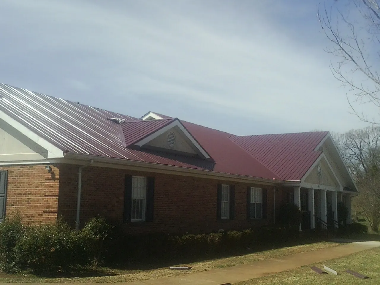 Red metal roof with gabled entries on a long brick building, from a Hail Damage Roof Repair job in Newton