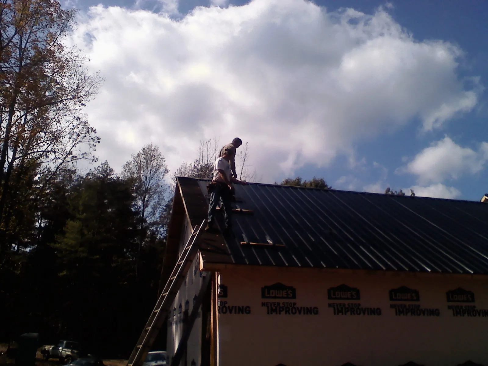 Roofer fastening dark metal panels high against a cloudy sky, from a Roof Inspection job in Newton